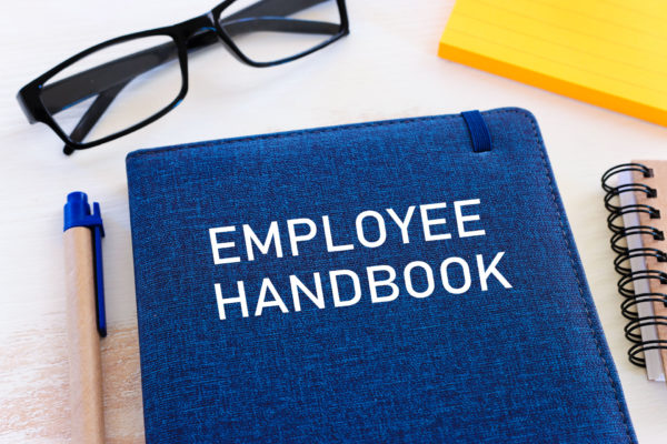 Employee handbook sits on desk next to pencil and glasses
