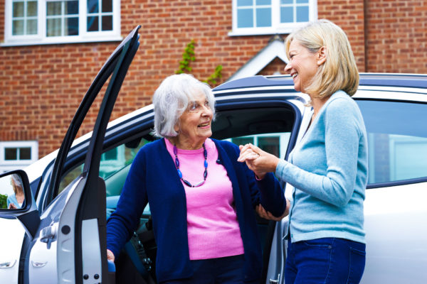 Woman helps her senior mother get into her car to drive