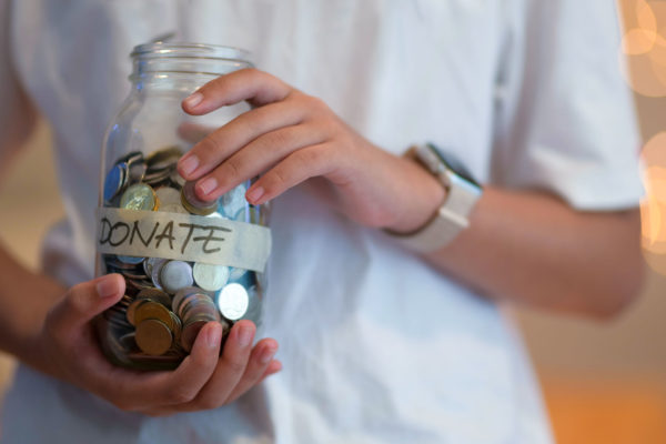Person holding coin jar labeled donations in preparation for charitable giving