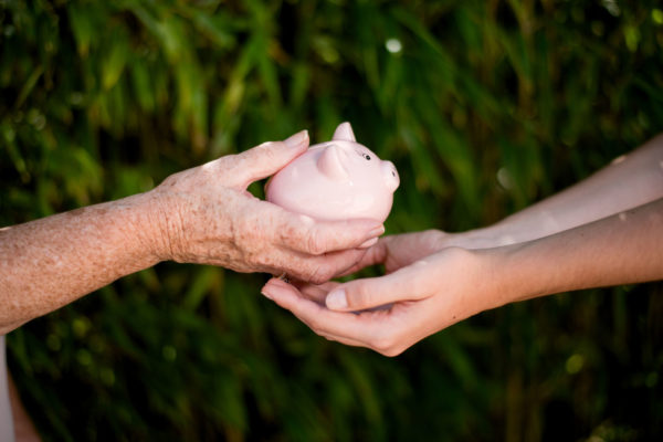 Elderly woman hands piggy bank to child as representation of business legacy transition