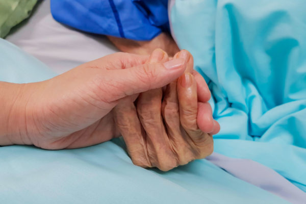 person holds hand of elderly parent during end-of-life care
