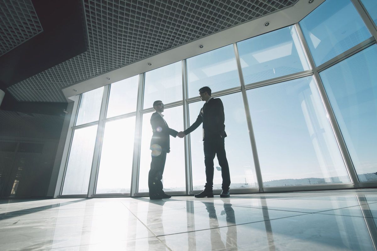 Two lawyers shaking hands in agreement in front of large windows.