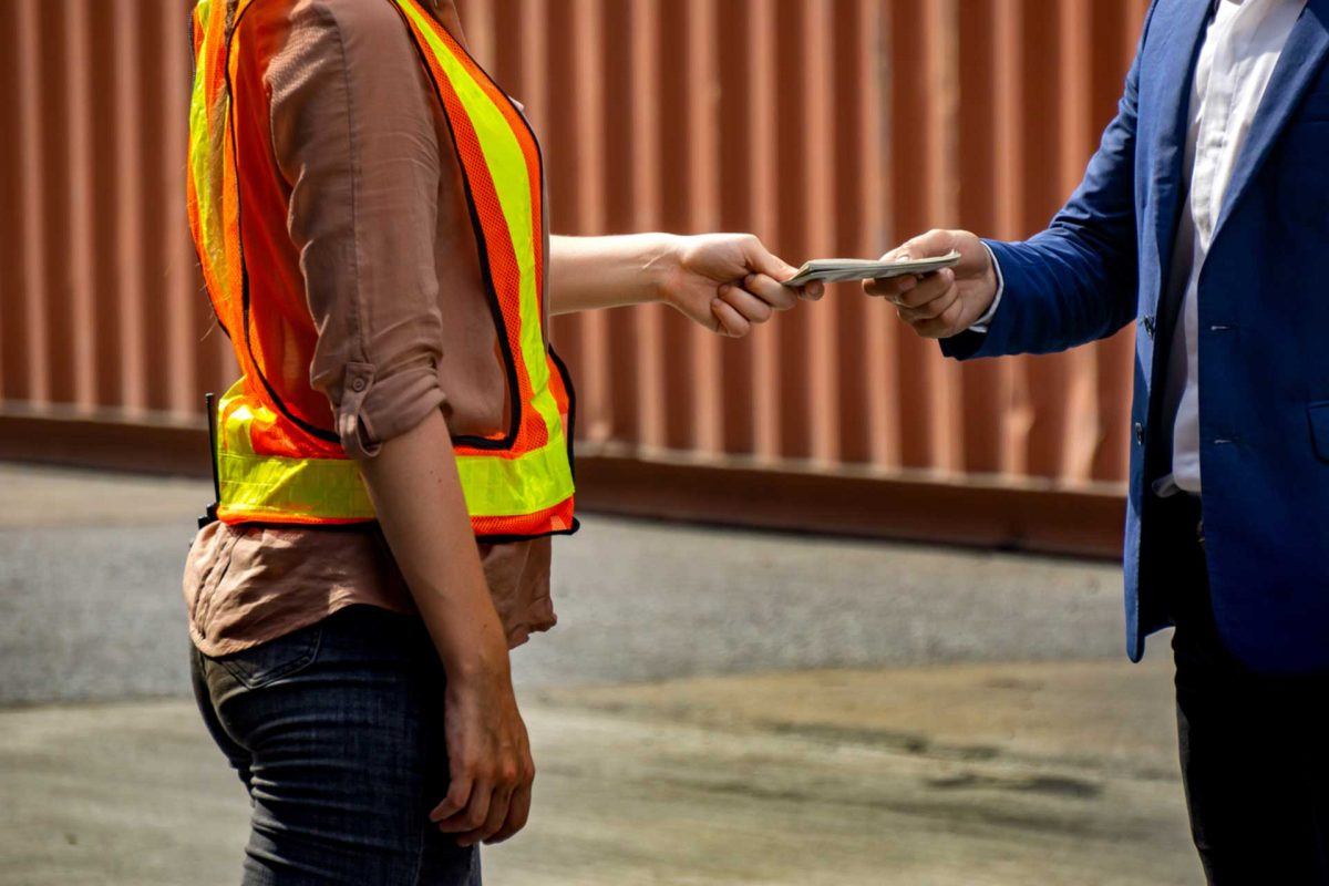 employer handing wages in cash to worker wearing hi-vis vest