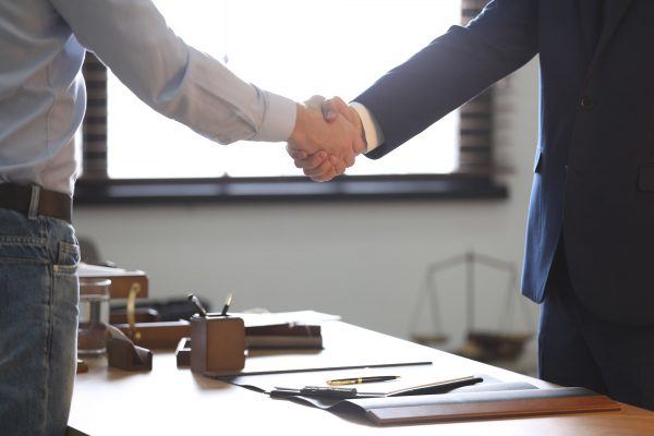 Male lawyer shaking hands with client over bypass trust in office, closeup